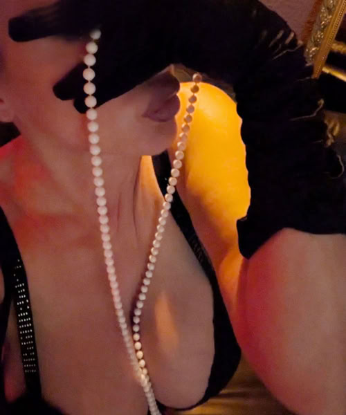 Celine at Flair Brothel Berlin wearing black gloves and holding a string of pearls, with a focus on the upper body and face partially obscured.