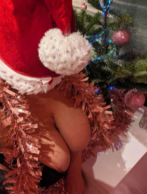 Celine wearing a Santa hat and surrounded by pink tinsel, sitting near a decorated Christmas tree with pink ornaments.