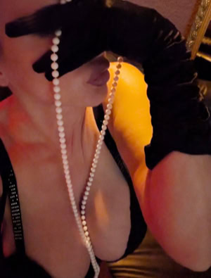 Celine wearing black gloves and holding a string of pearls, with a focus on the upper body and face partially obscured.