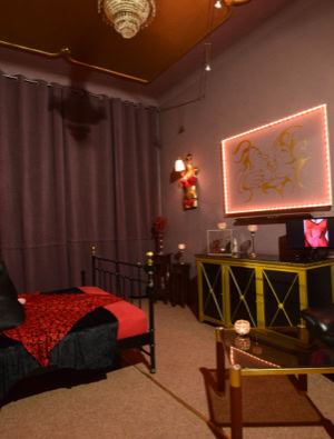 Zimmer 1 mit einem Bett, roter Bettwäsche, einem Spiegel, einem Sofa, einem Tisch und dekorativen Wandleuchten.