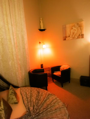 Gemütlich eingerichtetes Zimmer 3 mit zwei Sesseln, einem kleinen Tisch, einem Fernseher auf einem Schrank und warmem Licht.