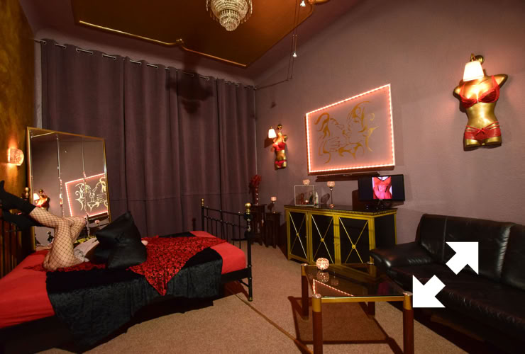 Flair Brothel Berlin with  dimly lit room with a bed, a mirror, a sofa, a small table, and wall decorations. The walls are purple, and there are red and gold accents throughout the room.
